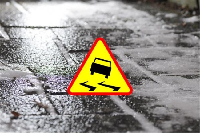 jezdnia, po środku znak drogowy ostrzegający przed śliską nawierzchnią drogi