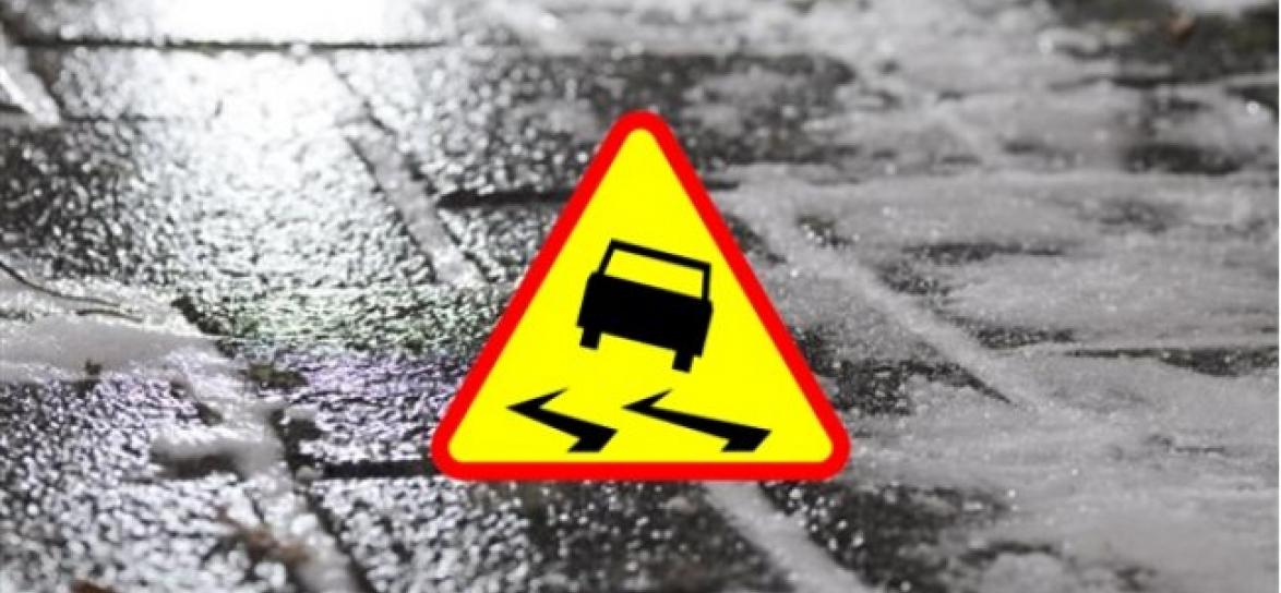 jezdnia, po środku znak drogowy ostrzegający przed śliską nawierzchnią drogi