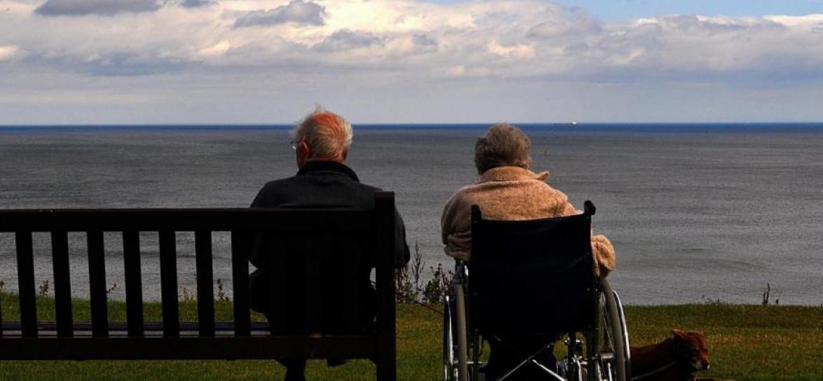 Osoba siedząca na ławce obok osoba siedząca na wózku inwalidzkim
